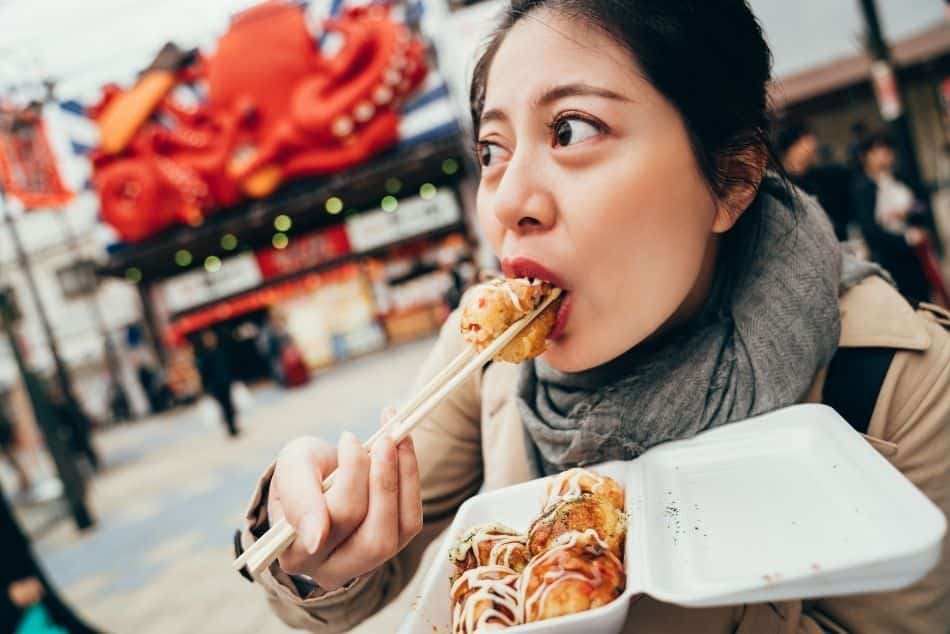 Lady eating takoyaki in a street in Osaka