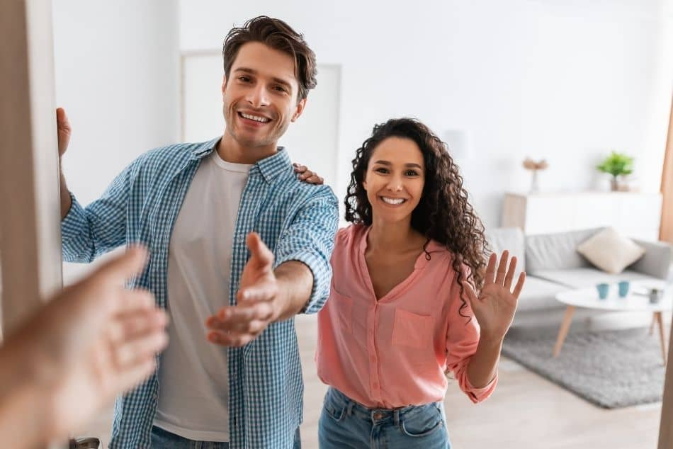 portrait-cheerful-couple-inviting-guests-to-enter-their-house